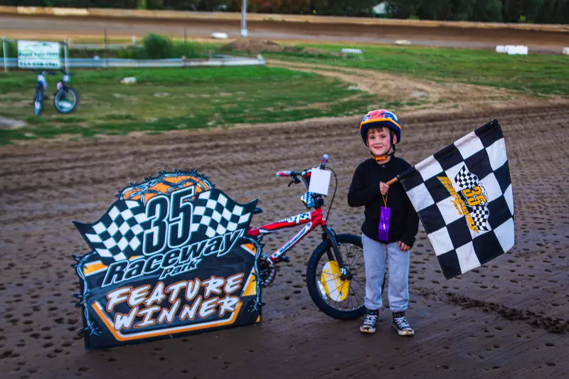 Young racer holding a checkered flag next to a feature winner sign