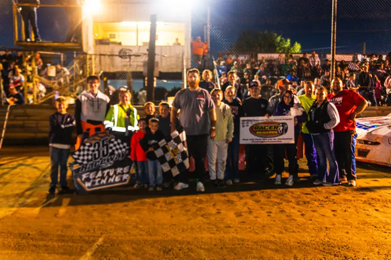 Drivers and crews celebrating in victory lane with banners and the checkered flag